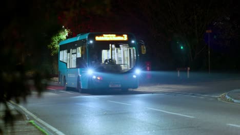a bus with headlights on drives towards and past the camera in a nighttime setting