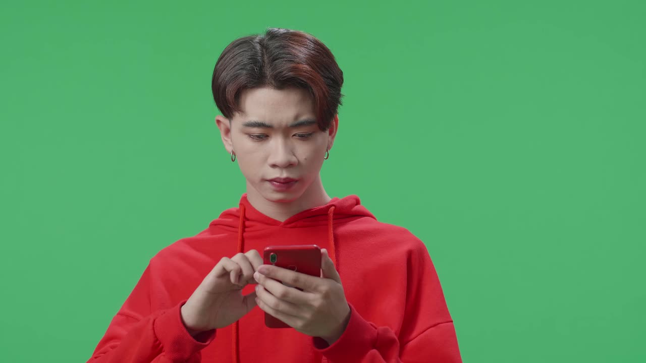 Young Asian Transgender Male Use Mobile Phone And Thinking About Something Then Raising Her Index Finger And Eyes Wide Open While Standing On Green Screen In The Studio