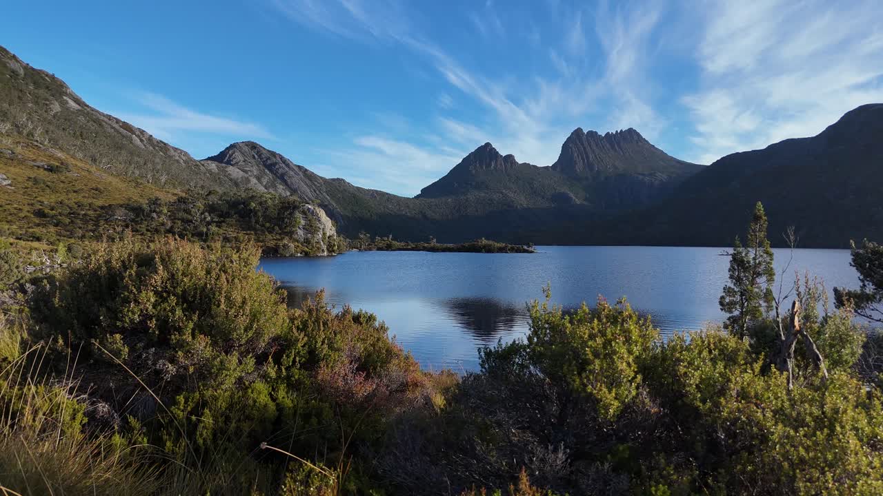 Ampia ripresa aerea del Lago Dove e di Cradle Mountain sullo sfondo. Giornata di sole con vegetazione verde in Tasmania, Australia. Natura selvaggia e area patrimonio dell'umanità. Ripresa laterale a bassa angolazione.