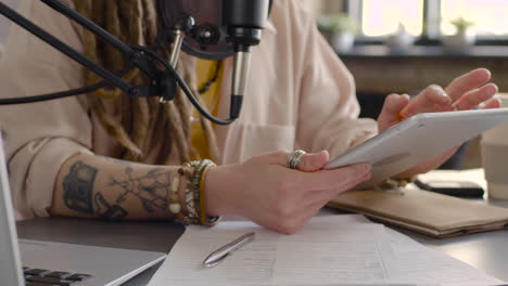 close up view of woman hands holding and tapping on a tablet while recording a podcast talking into a microphone