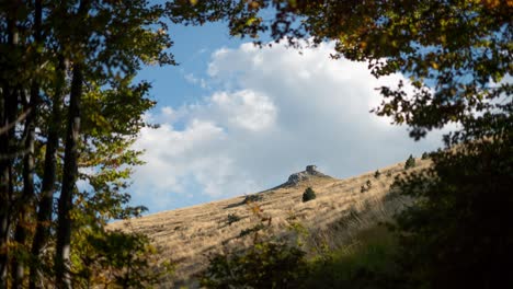 Timelapse-clouds-moving-over-mountain-peak-surrounded-by-deep-forest-trees-day