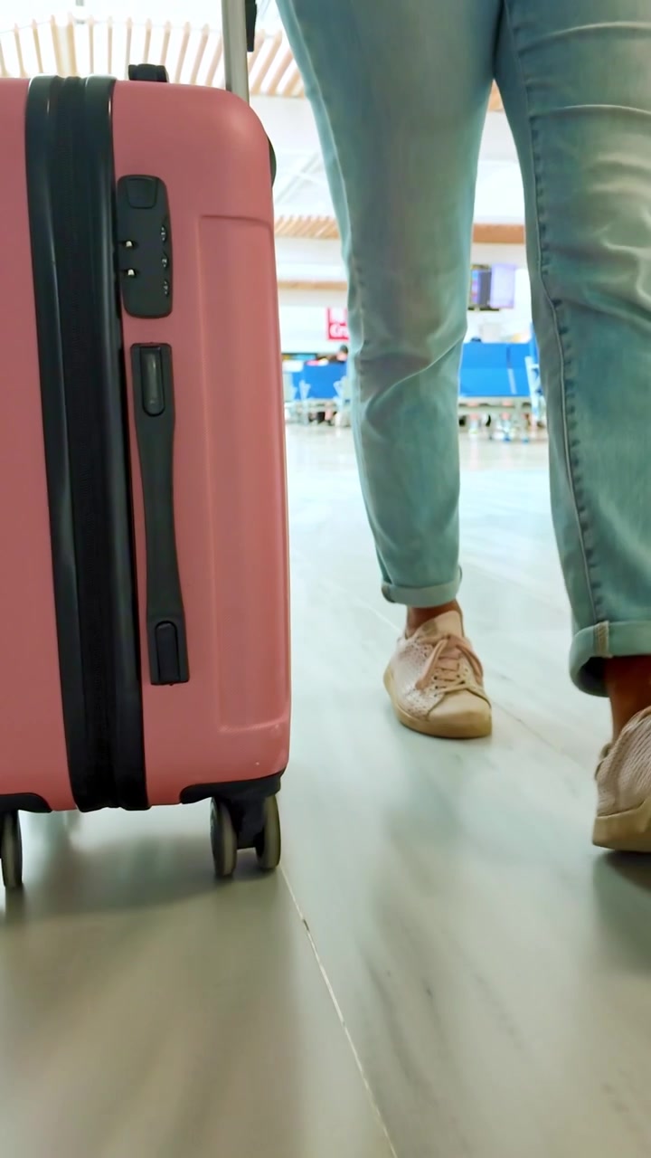 Mujer con maleta rosa caminando en la terminal del aeropuerto