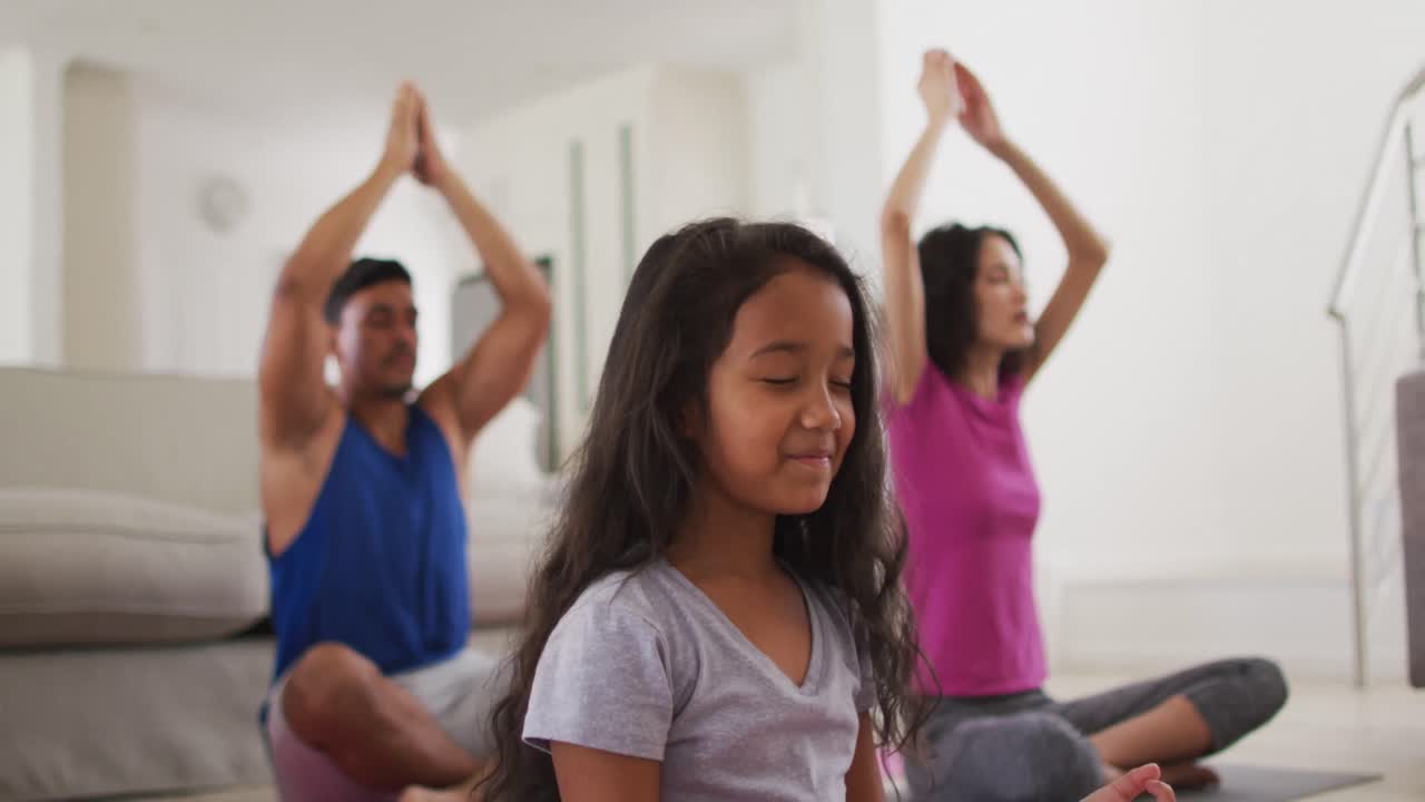 padres hispanos e hija sentados en el suelo meditando en casa