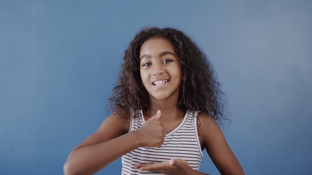 chica afroamericana feliz usando lenguaje de señas en fondo azul, cámara lenta