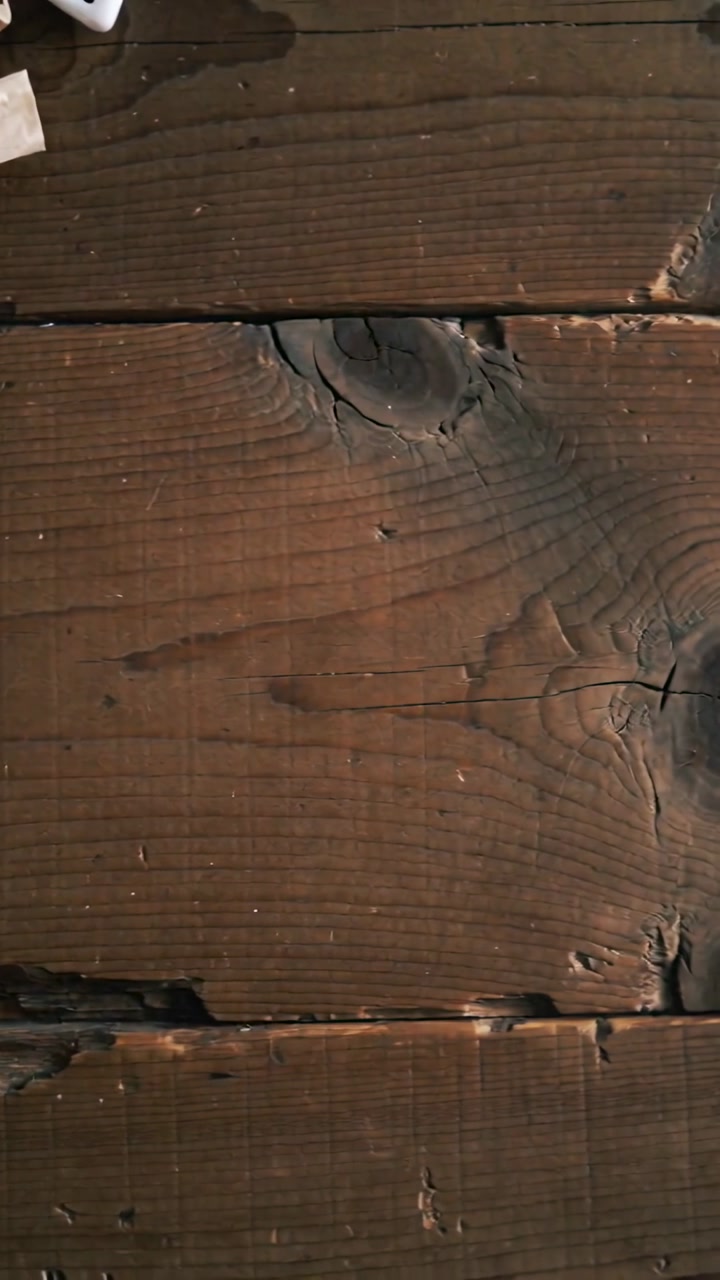Vertical video: Sliding camera revealing worn dark wooden planks at cafe, showing mug napkin crumbs