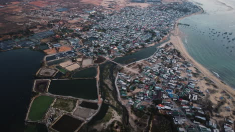 aerial shot of famous son hai town in southern vietnam with popular shrimp farming pools - rotating wind turbines in background - beautiful coastline with sandy beach and ocean in vietnam - ascending