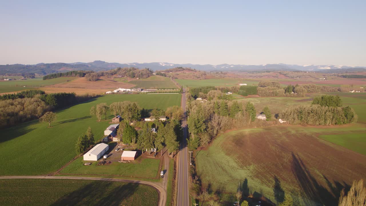 dolly reverso aéreo sobre a luz dolden hour na estrada secundária, campos em ambos os lados