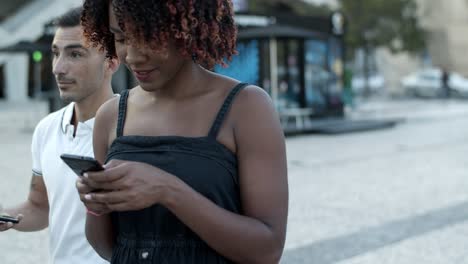 una mujer afroamericana sonriente caminando con un teléfono inteligente