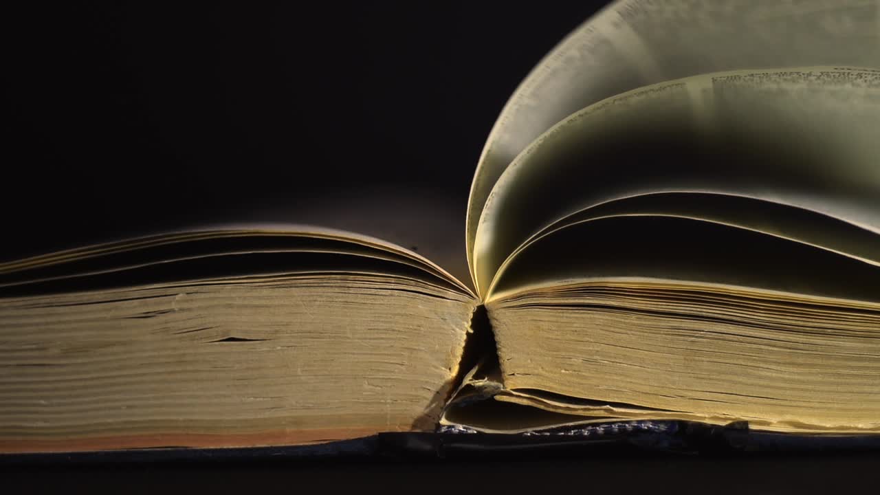 Rallentatore, primo piano di un libro antico, vintage, aperto con le pagine che si girano al vento, in una stanza buia con poca luce e sfondo nero