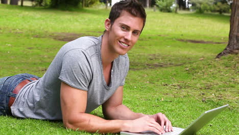 man typing on a laptop before looking at the camera and smiling