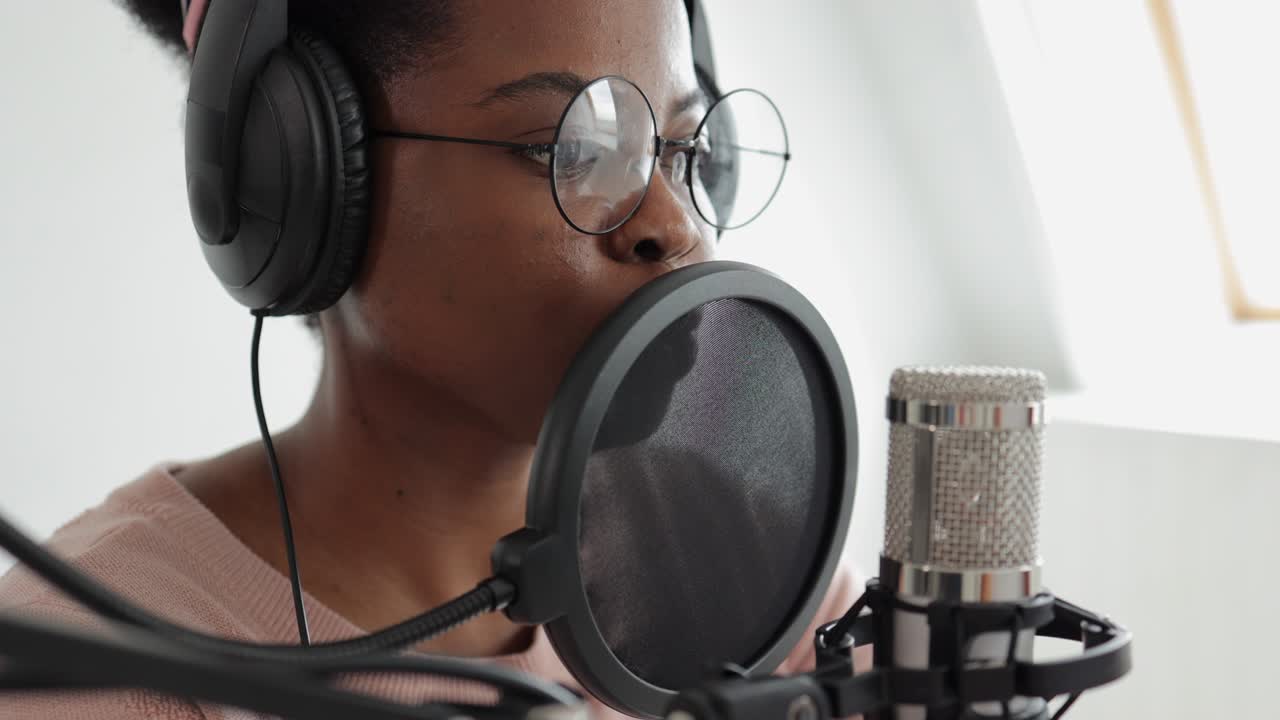 Creazione di podcast e contenuti audio, una donna afroamericana sicura di sé e bella con un microfono e delle cuffie che registra un podcast in uno studio di registrazione o a casa sua.