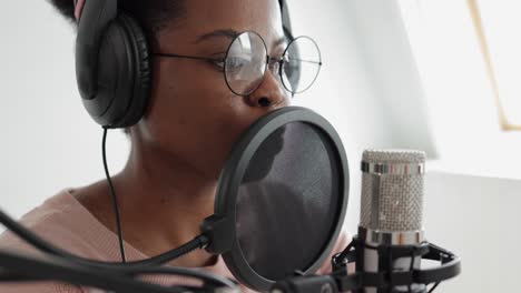 podcast and audio content creation, confident and beautiful african-american woman with a microphone and headphones recording a podcast in a recording studio or in her home
