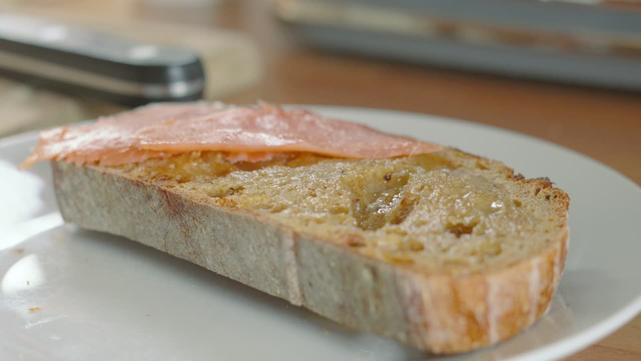 Female Chef Laying Slices of Smoked Salmon on Rustic Sourdough Bread on Plate with Kitchen Utensils in Background