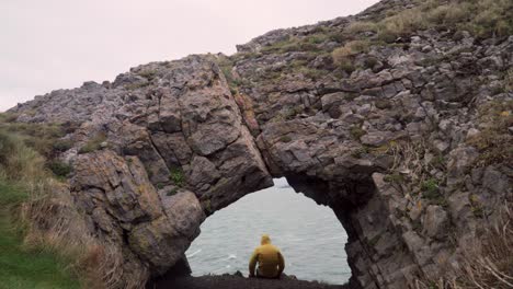 man looks out to sea in cave - yellow jacket