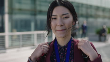 close-up-portrait-of-young-asian-business-woman-looking-to-camera-hair-blowing-in-wind-smiling