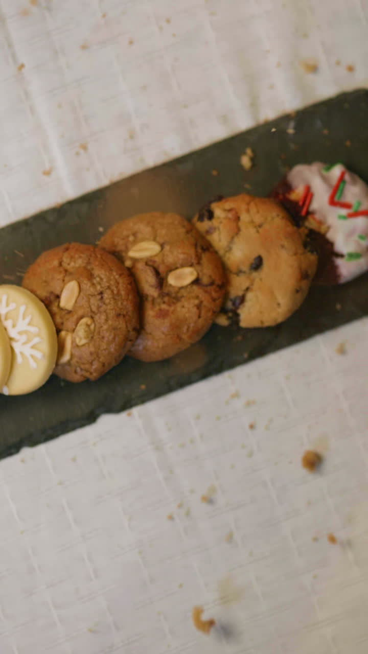 Variety of Christmas cookies on a rotating chalkboard with crumbs falling, showing festive details and decorated textures