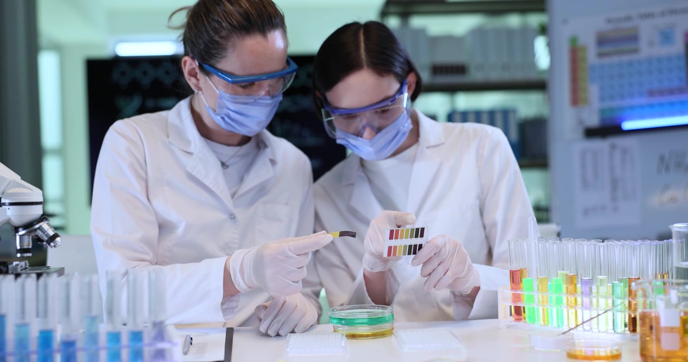 Lady chemists conduct test liquid ph with reagent and color scale