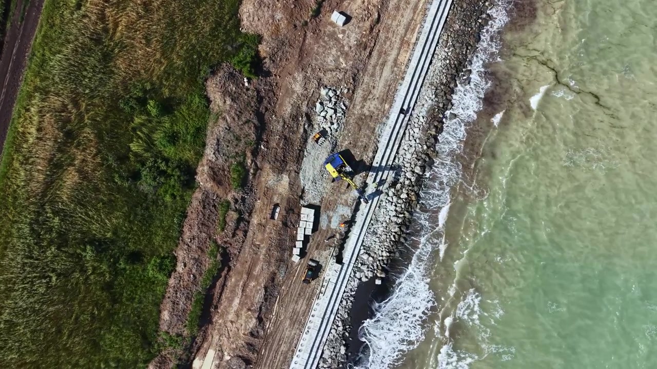 Lavori di costruzione in un'area costiera con macchinari e materiali vicino all'acqua durante le ore diurne