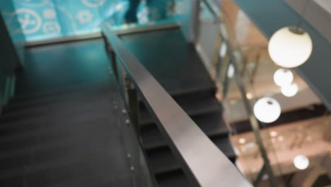 first-person view capturing the staircase with modern glass railings and the surrounding indoor environment. the camera focuses on the sleek design of the stairs and the bright, decorated background