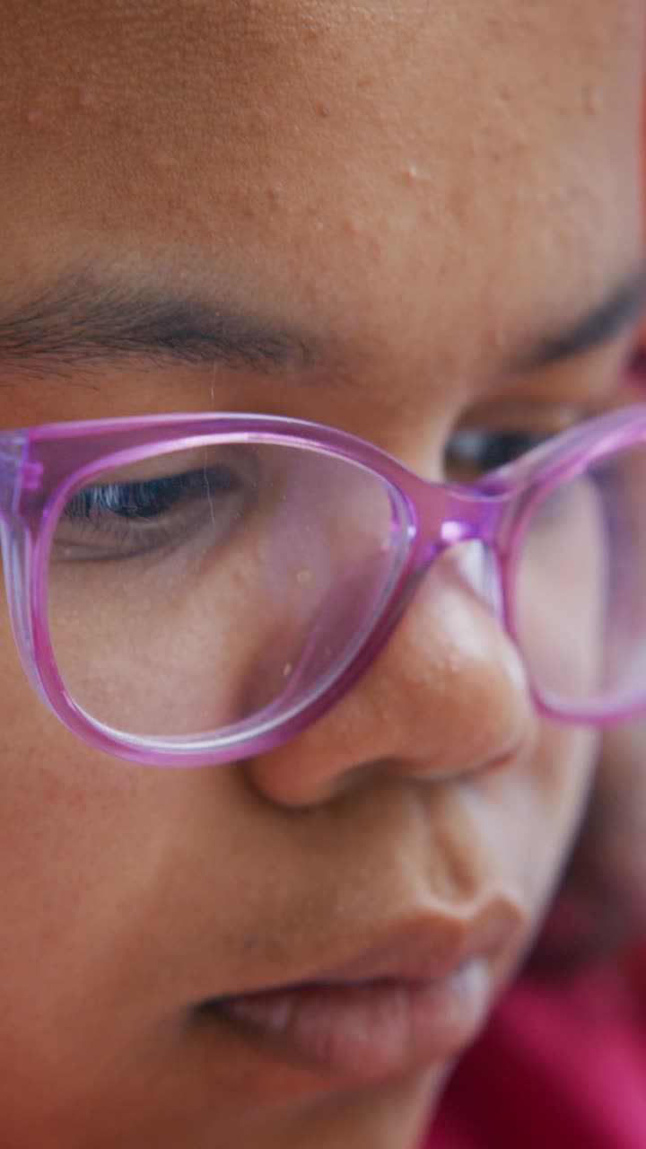 Giovane ragazza con gli occhiali viola che guarda in basso con attenzione