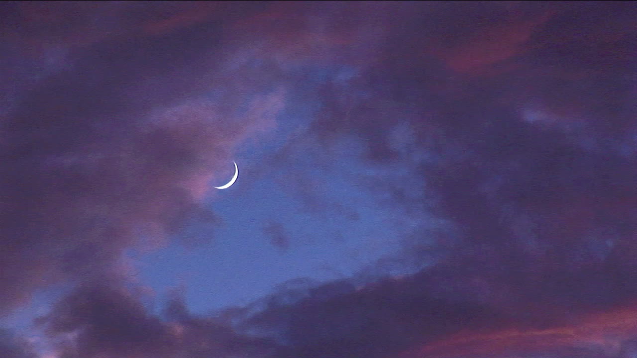 nubes teñidas pasan junto a una luna creciente a la hora dorada