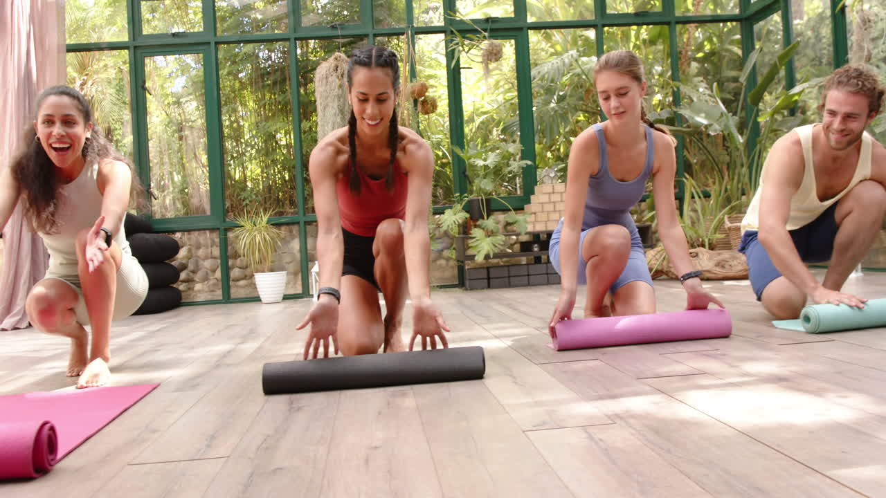Rolling out yoga mats, group preparing for yoga session in glass house studio