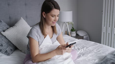 mujer sonriendo y usando el teléfono en la cama