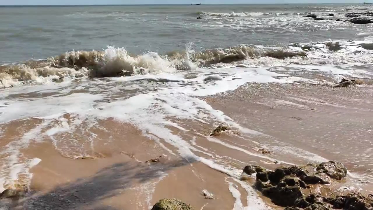 Milde havbølger som ruller inn på en sandstrand med steiner