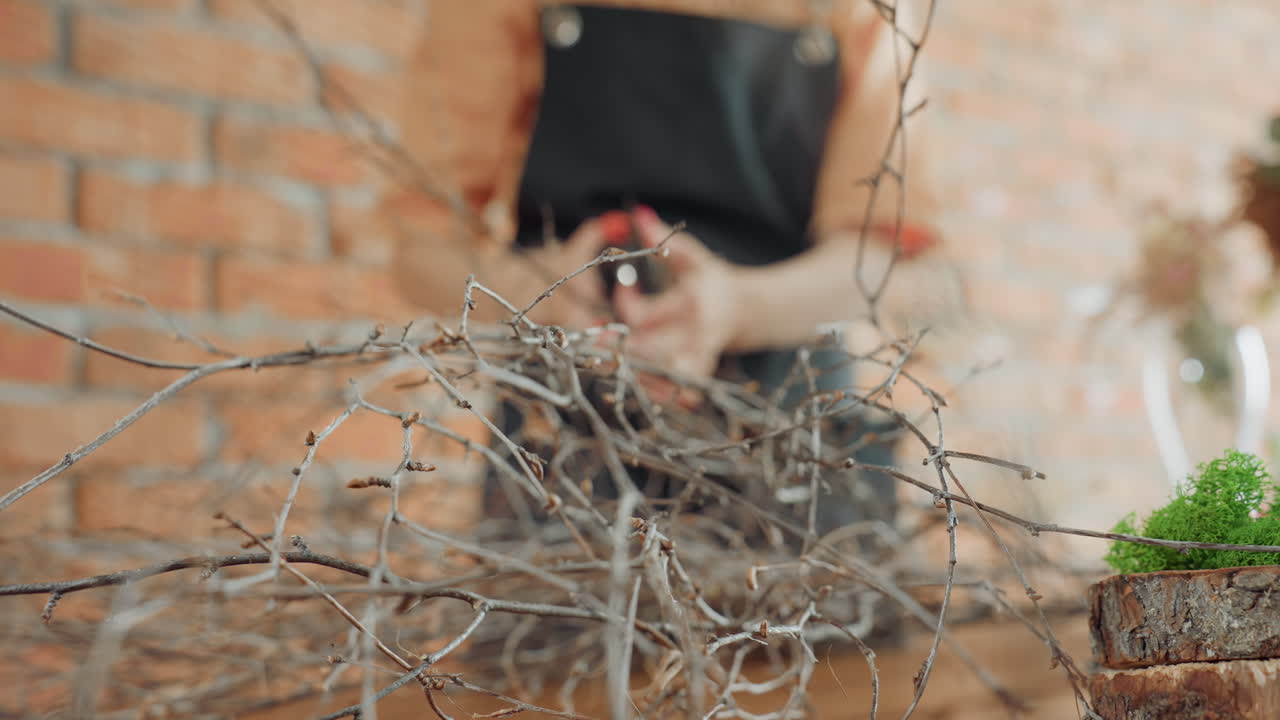 Closeup view of dry twigs arranged on wooden table with vibrant green moss and rustic wood slices in foreground, representing natural materials for handmade floral or seasonal decoration project