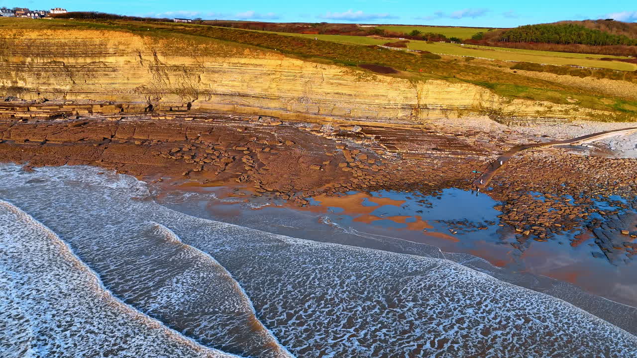 Vista aérea de falésias de calcário e praia rochosa em Southerndown. Vista de cima das falésias da Baía de Dunraven e das piscinas naturais durante a luz dourada do pôr do sol no País de Gales.