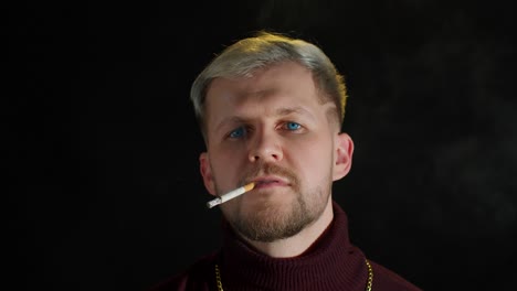 Stylish-addicted-young-man-with-blue-eyes-in-trendy-clothes-looking-at-camera,-smoking-cigarette