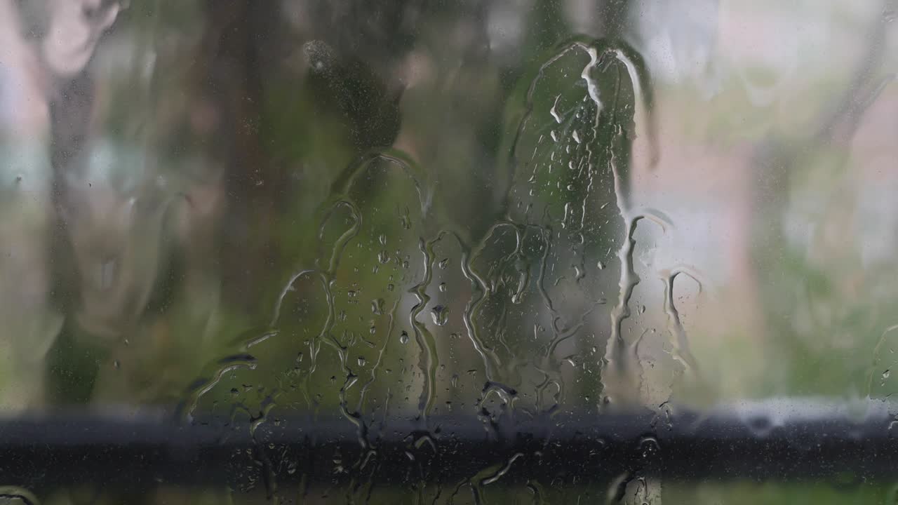 Strong rain water flushes against window glass and streaming down. Close-up. Raindrops on glass background in rainy season. 4k