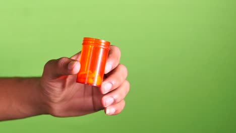 close up de un hombre con la mano sosteniendo un recipiente de pastillas en la pantalla verde