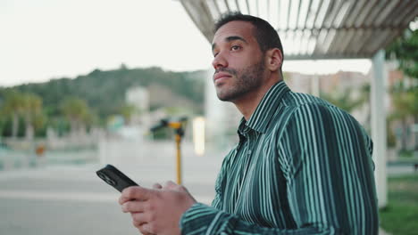 Young-man-texting-on-smartphone-sitting-in-bench-outdoors.