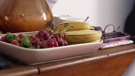 Ein-Schwebender-Schuss-Erdbeeren,-Bananen-Und-Weintrauben-Auf-Einem-Tablett,-Auf-Einem-Beistelltisch-Sitzend