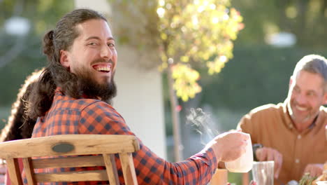 Happy-diverse-male-and-female-friends-eating-thanksgiving-celebration-meal-in-sunny-garden