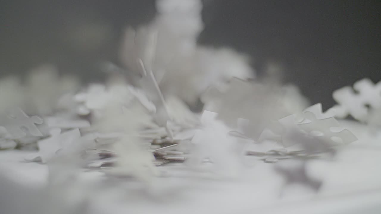 Slow motion: White and gray puzzle pieces falling on a white surface and bouncing and spinning back with a dark background. Close up with shallow depth of field. Shot in 4K
