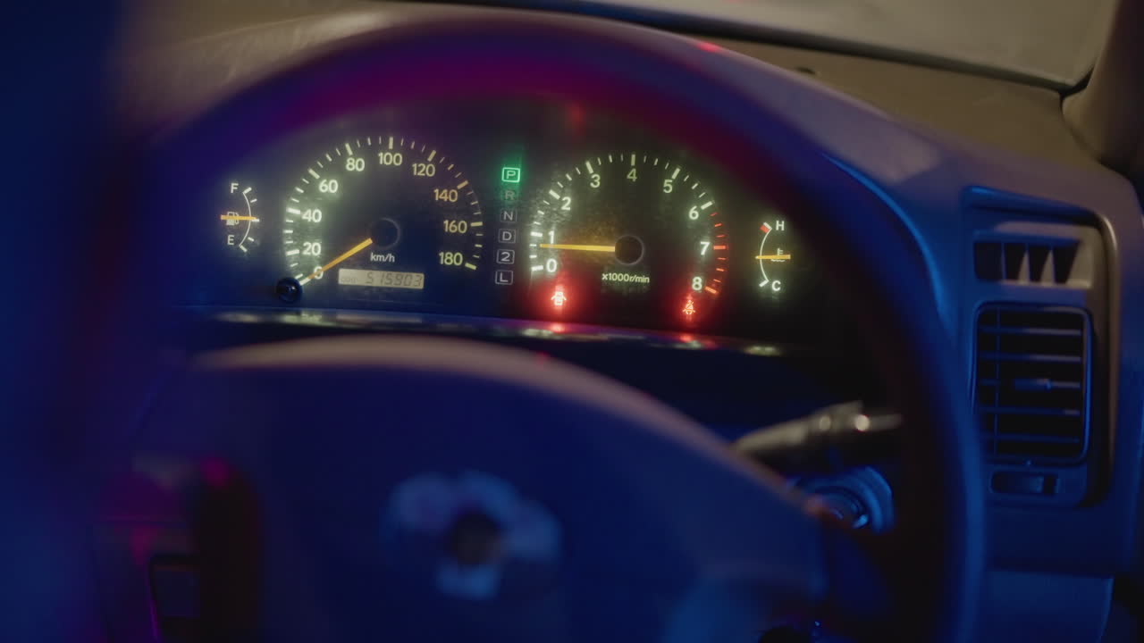primer plano del salpicadero de un coche de noche que muestra las luces de advertencia y el agarre del volante, un conductor solitario mira las alertas rojas y verdes parpadeantes mientras la aguja del velocímetro se mantiene fija, reflejos azules y púrpuras de neón lo inundan todo