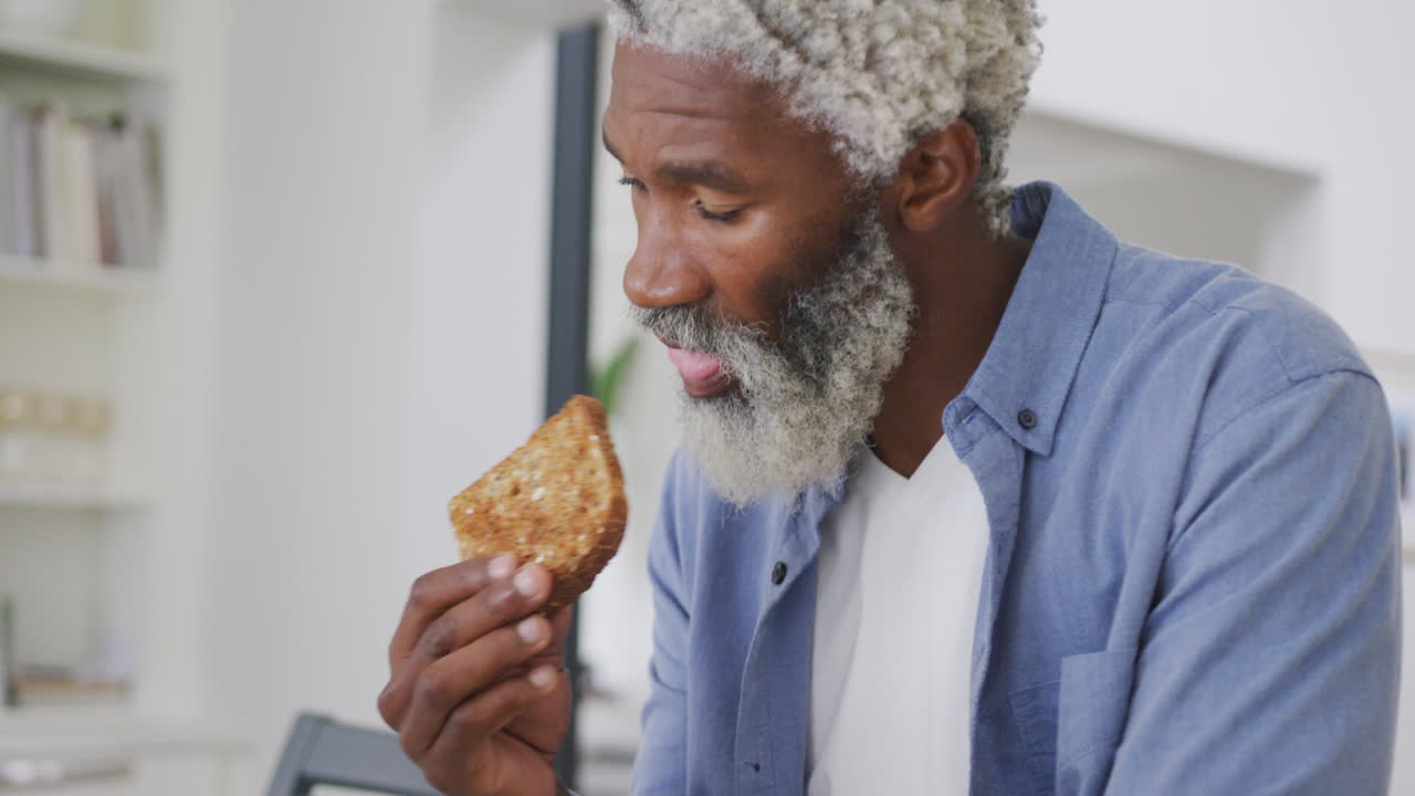Video of sad african american senior man with eating toast