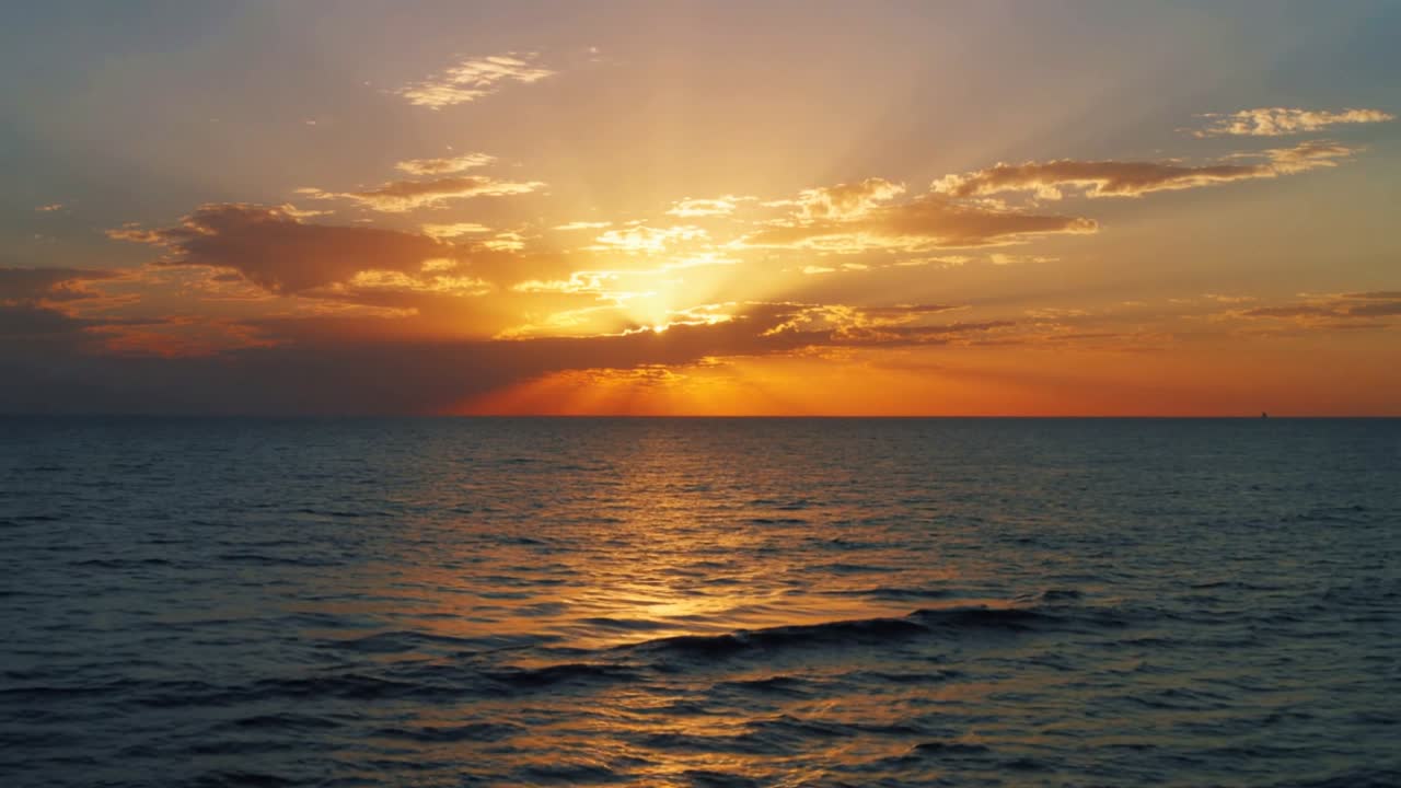 Sun descending at sunset, casting rays through clouds and creating bright glint on water for design