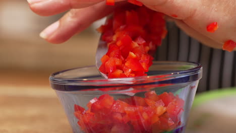 midiendo una porción de pimientos rojos picados para una receta casera - cámara lenta aislada