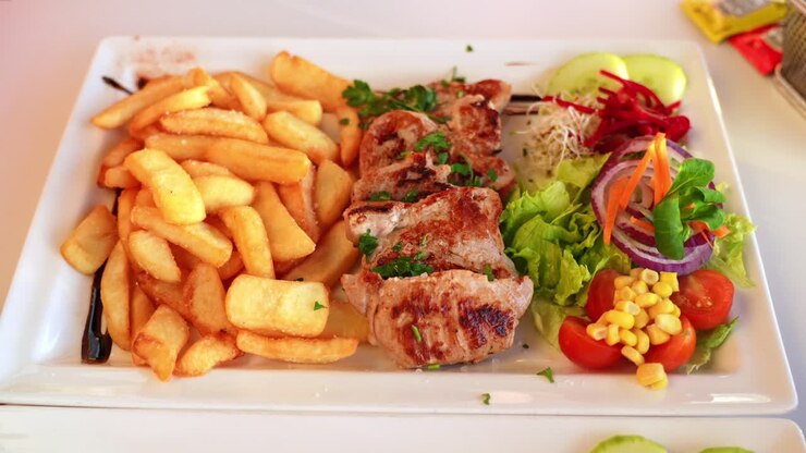 Comida equilibrada con carne, patatas y verduras coloridas: Solomillo de cerdo a la parrilla con patatas fritas doradas y ensalada fresca.