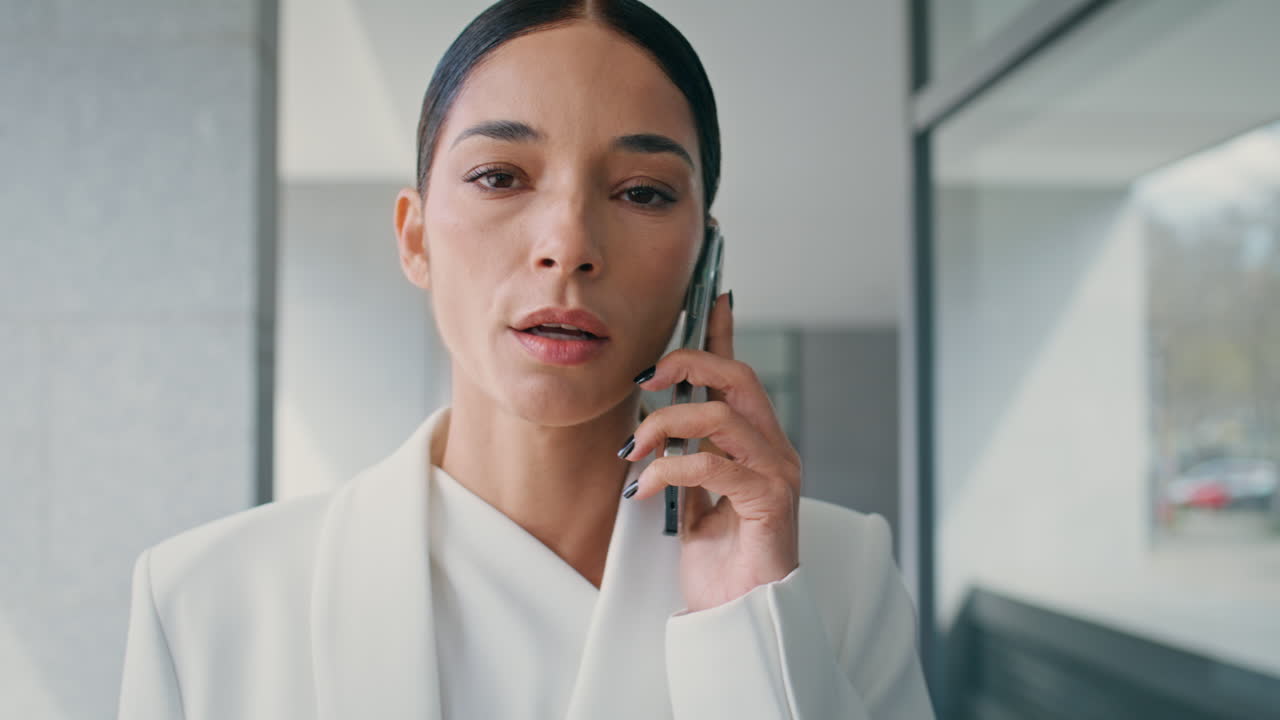 짜증나는 사업가 여성이 전화를 하고 사무실 복도를 걸어서 근접으로 일하고 있습니다.