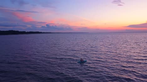 una toma dramática de un dron de un kayakista solitario deslizándose lentamente hacia una puesta de sol colorida
