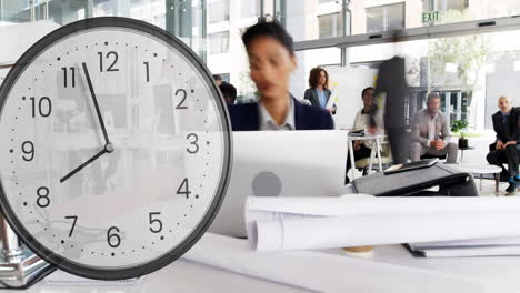 Animation-of-clock-ticking-over-biracial-businesswoman-in-office