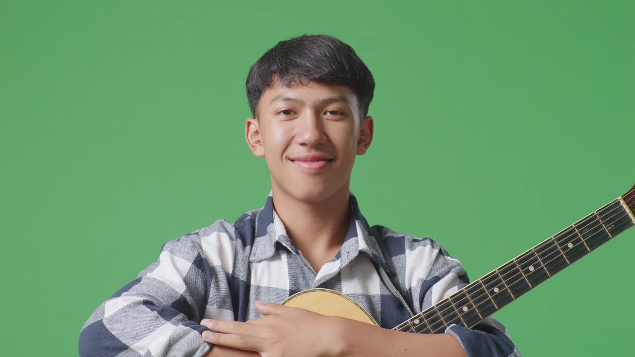 기타를 들고 팔을 고 초록색 스크린 배경에 미소 짓는 아시아 십대