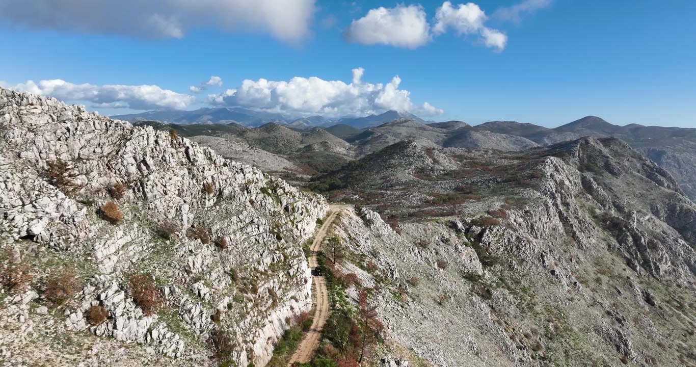 Terreno roccioso vicino a Dubrovnik con scogliere a picco e ampie viste montuose mentre un veicolo fuoristrada si avvicina al punto panoramico, tracciamento aereo