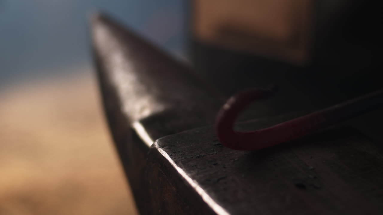 대장장이는 작업장에서 망치로 모루에 구부러진 금속 장식을 작업합니다