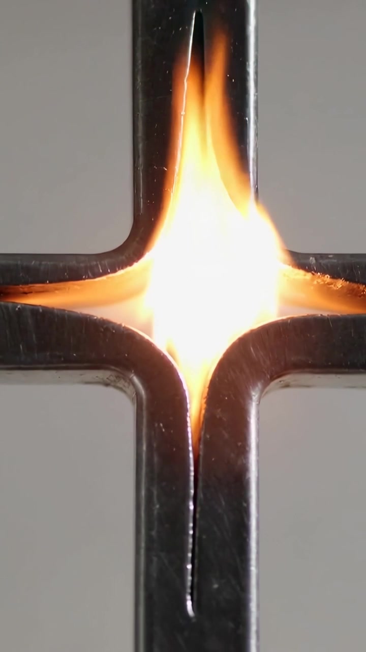 Vertical video: Seam fuel igniting, metal cross bearing flickering flame in studio, scorched metal