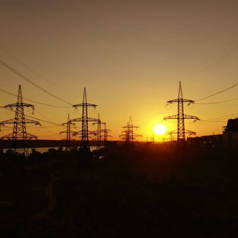 silhouette of electric towers against orange sunset. high-voltage electric lines among the evening nature. electricity efficiency. transmission lines and factory.